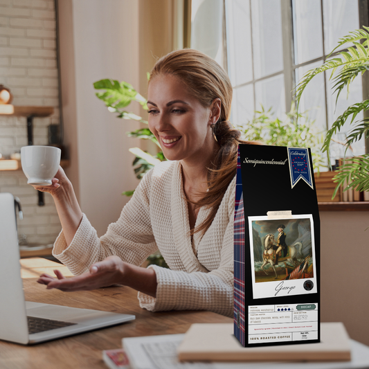 Image of woman enjoying a cup of coffee while working on her laptop with a box of George specialty coffee on her desk.